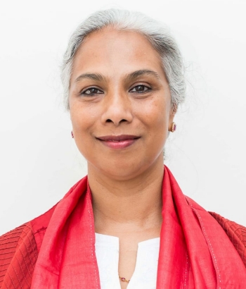 Smiling woman with short, silver hair, wearing a white shirt and red cardigan and scarf