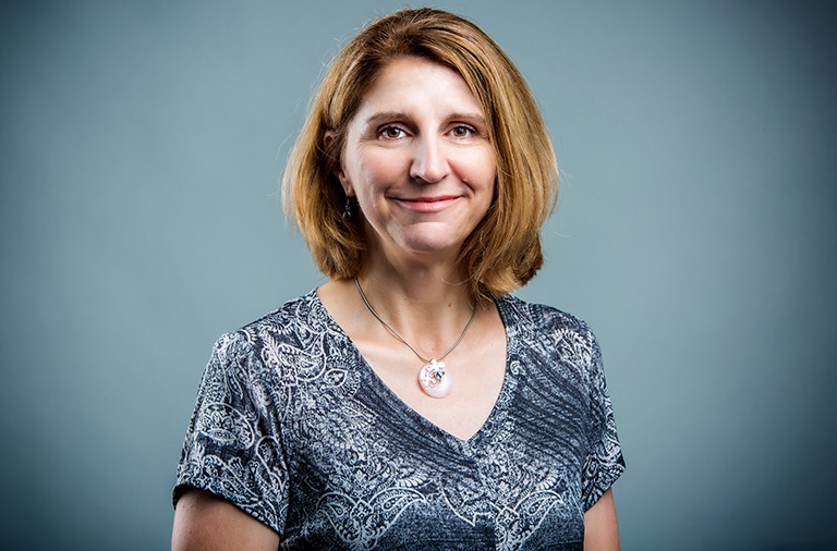 Smiling woman with shoulder-length brown hair with a necklace and short-sleeved shirt.