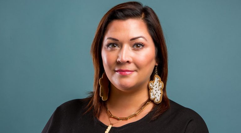 Smiling woman with shoulder-length dark hair, wearing large beaded earrings, a necklace and a black top.