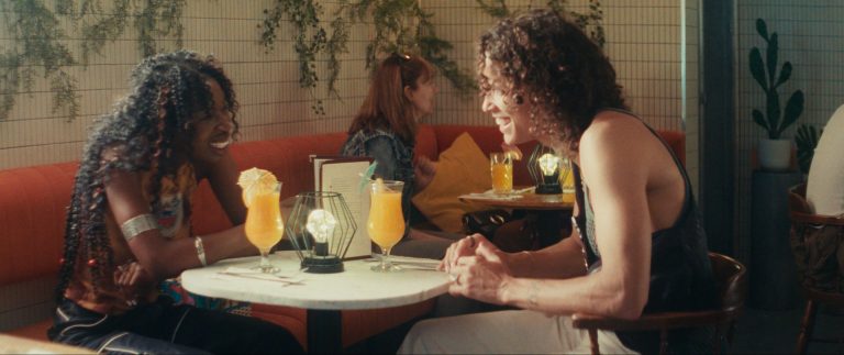 Two people talking to each other and seated at a table in a cafe.