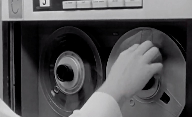 A hand touching the reel of an old audio recording machine.