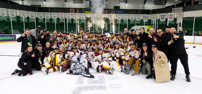 A women's sports hockey team on the ice, gathered together for a group photo, celebrating a win at Nationals.