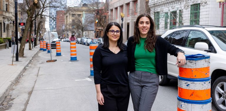 Sadaf Gharaati and Rebecca Dziedzic stand by a striped orange pylon in downtown Montreal