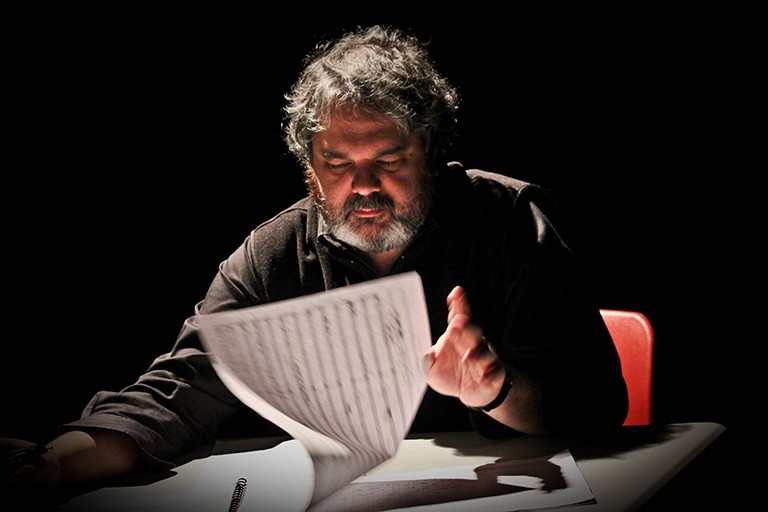 Man with grey hair and beard, reading pages of music