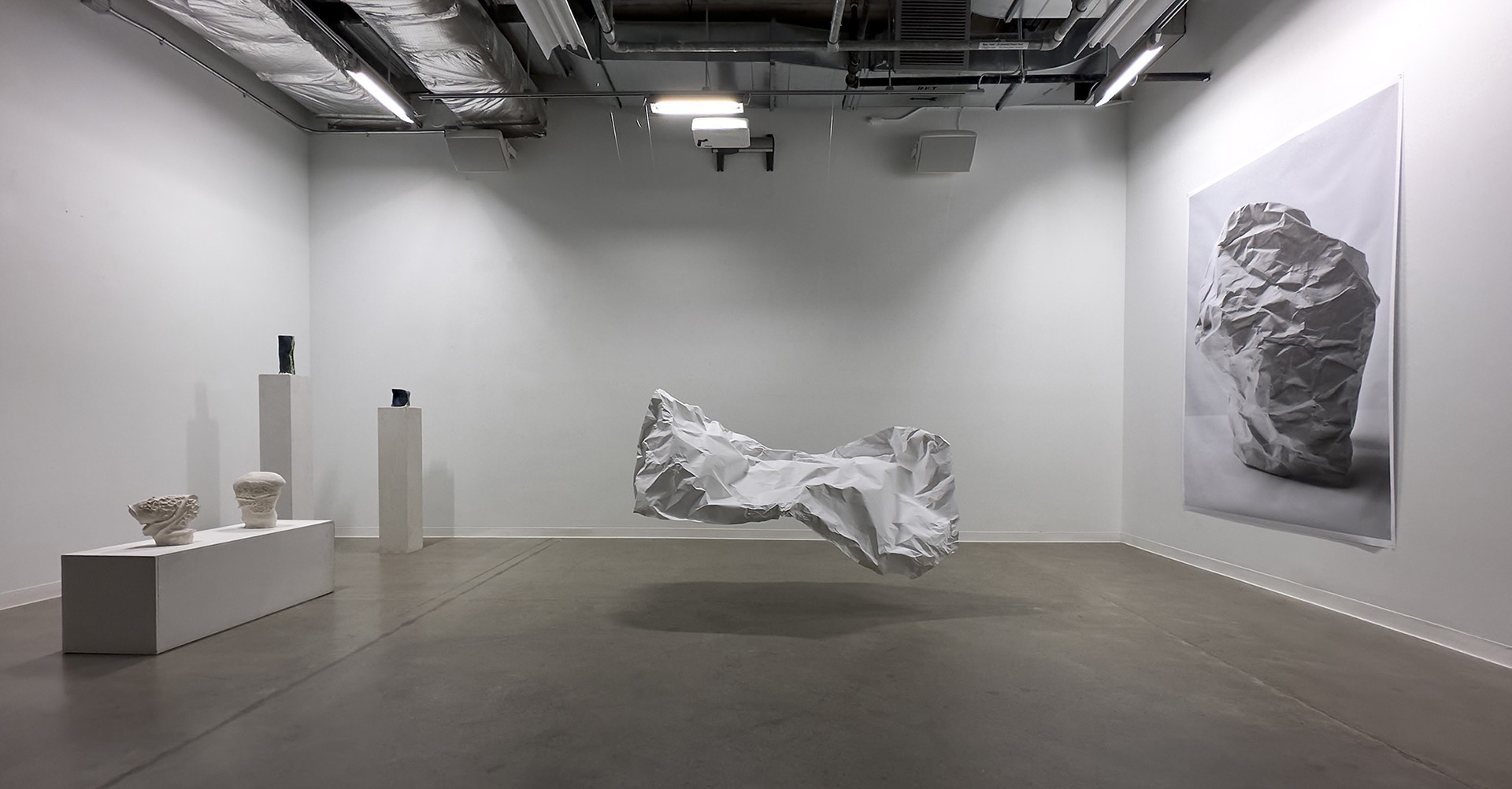 Exhibition installation of artistic pieces — small sculptures and a larger piece shaped like crumpled paper.