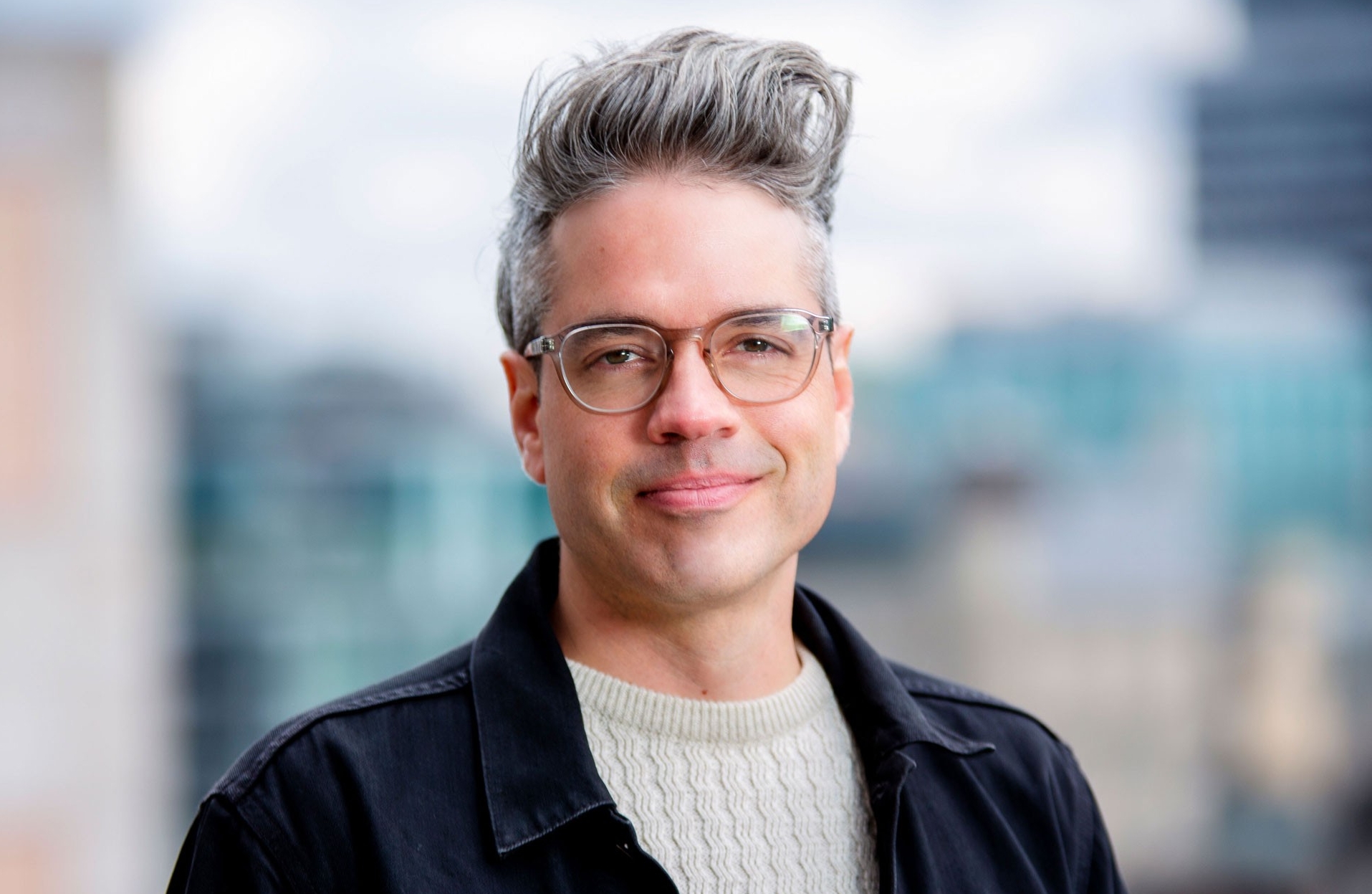 Middle-aged man with grey hair and glasses, smiles at camera