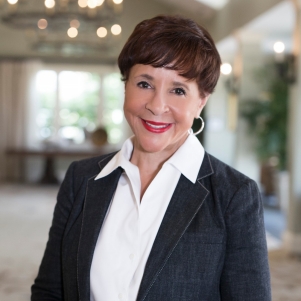 Smiling woman with short, dark hair wearing a white shirt and black blazer