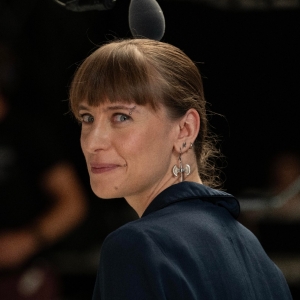 Smiling woman with dark blonde hair, looking back over her shoulder, and wearing a dark grey shirt.