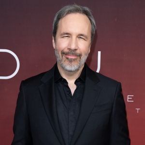 Smiling man with short grey hair and beard, wearing a black suit