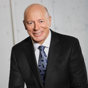 Smiling bald man in a dark grey suit, smiling for the camera