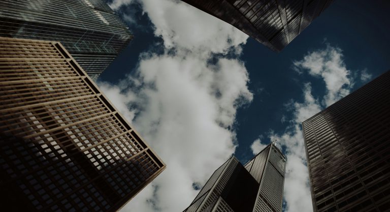 City buildings seen from below, with blue sky and clouds above