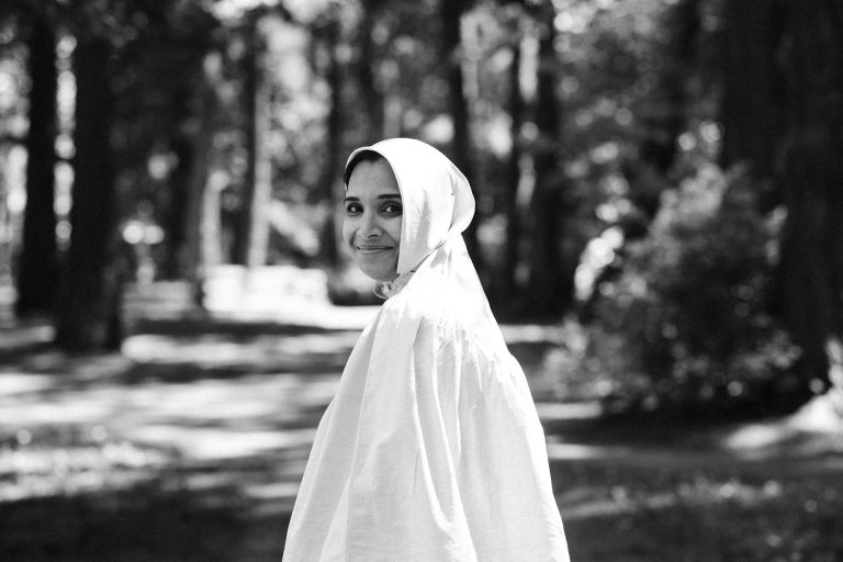 Woman dressed in white smiling at camera over her shoulder while walking in forest