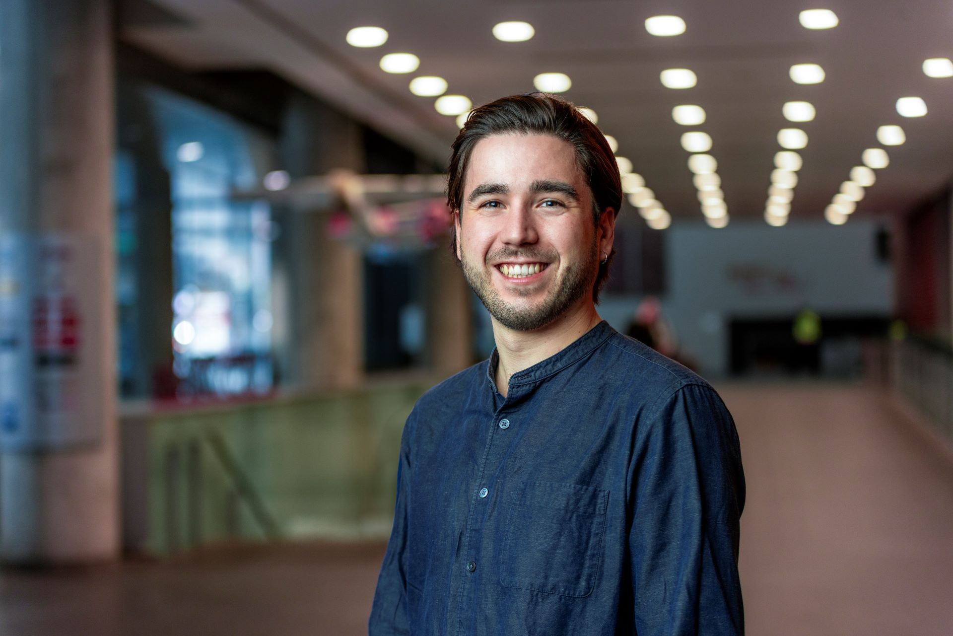 Hugo Jourde A young man in a blue shirt smiles in a university corridor