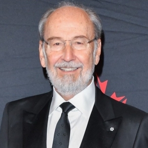 Smiling man with sparse grey hair, a grey beard and wearing a suit and black tie.