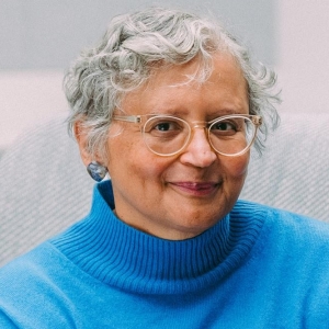 Smiling woman with dark blonde hair, looking back over her shoulder, and wearing a dark grey shirt.
