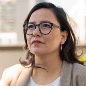 A smiling woman wearing dark-rimmed glasses, looking up and to the left of the frame.