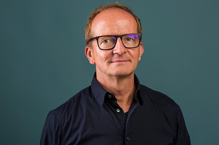 Jens Richard Giersdorf: “We are incorporating an understanding of the political potential of dance in society.” Smiling man with short, reddish hair, wearing dark-rimmed glasses and a navy blue button down shirt.