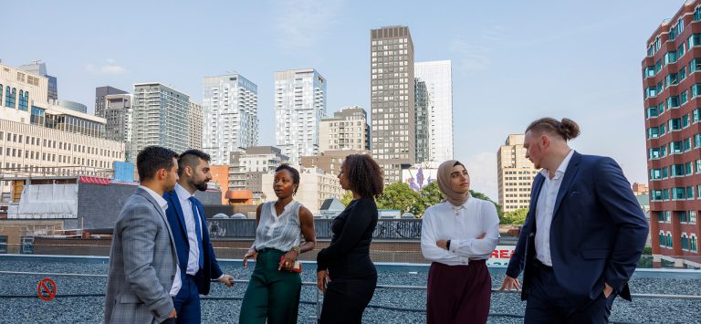 A group of diverse people standing on a roof terrace in a city scape.