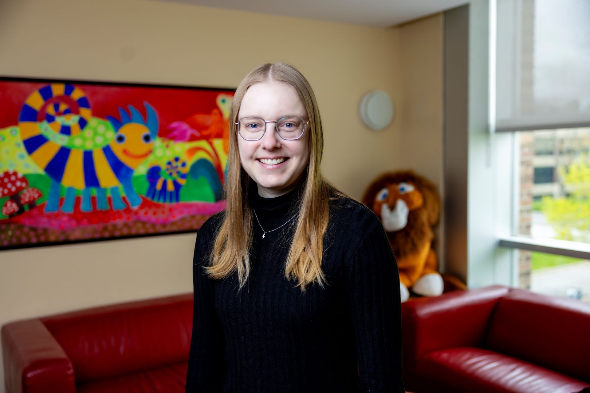 Marilyne Dragon A young woman with long hair and glasses in a black sweater