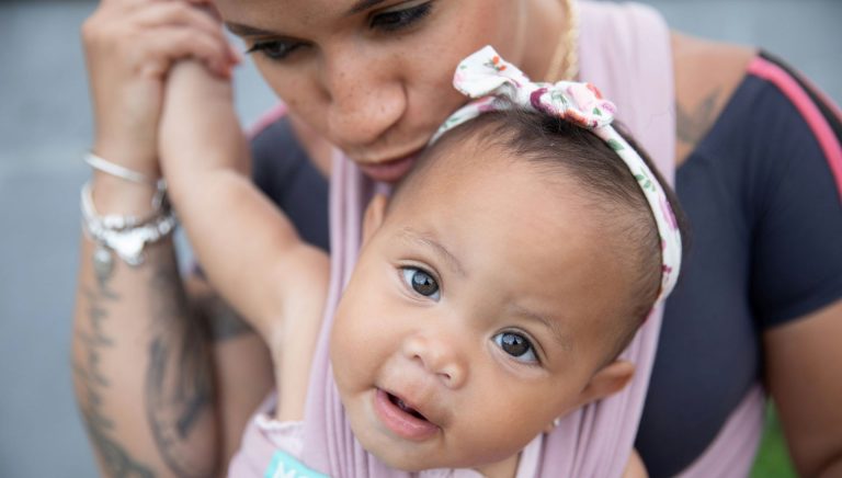 A woman holds a toddler in a baby carrier