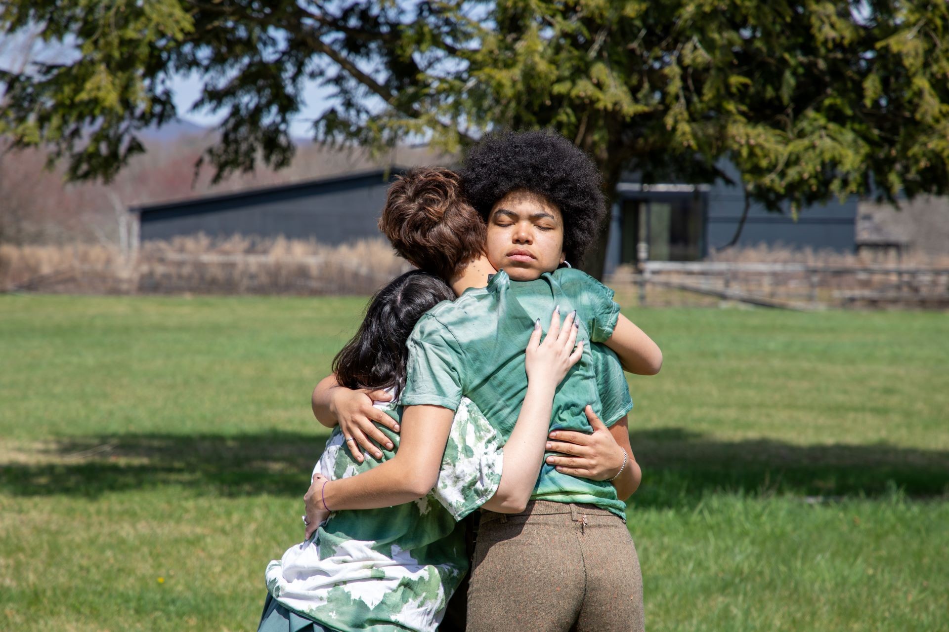 How do we remember places that the sun can’t touch? at Boisé Steinberg. | Photo by Christine White Three women hug in a field