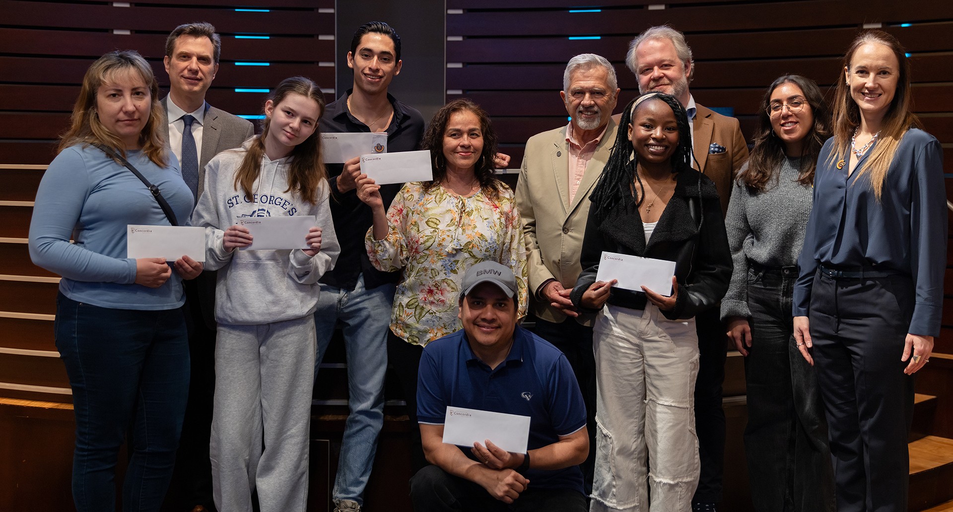 A group of people standing together and holding envelopes while smiling to the camera.