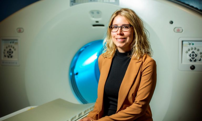 A woman in glasses sits in front of an MRI machine