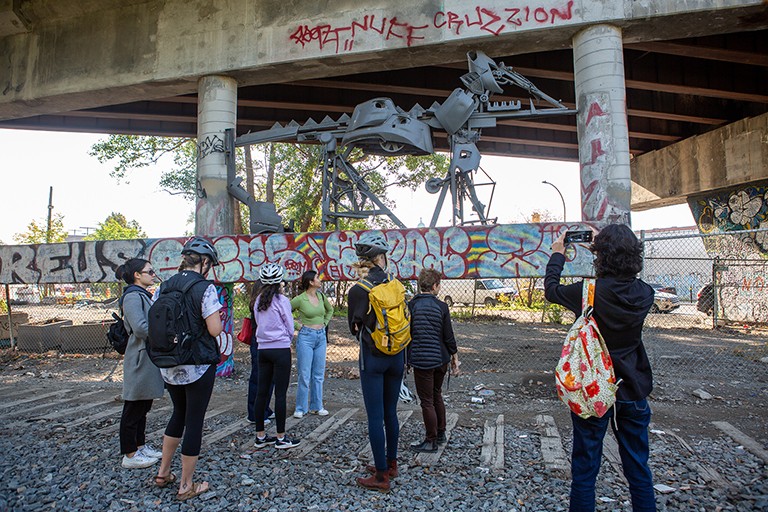 A group of people standing looking at graffiti in an urban setting underneath an overpass