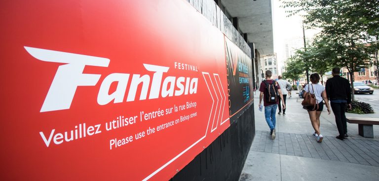 A large red sign on the side of a building with the word, "Fantasia," on a busy urban street.