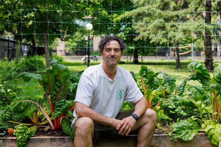 A smiling man in shorts and a white T-shirt sitting on the edge of a garden