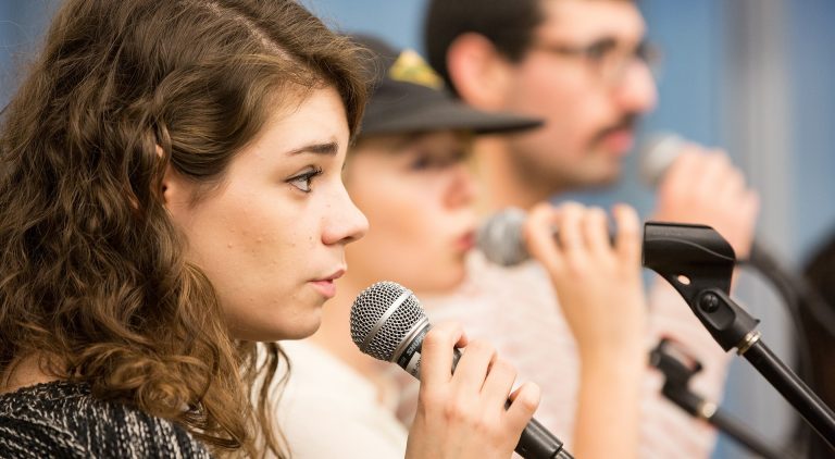 Side profile of two women and a man singing into microphones