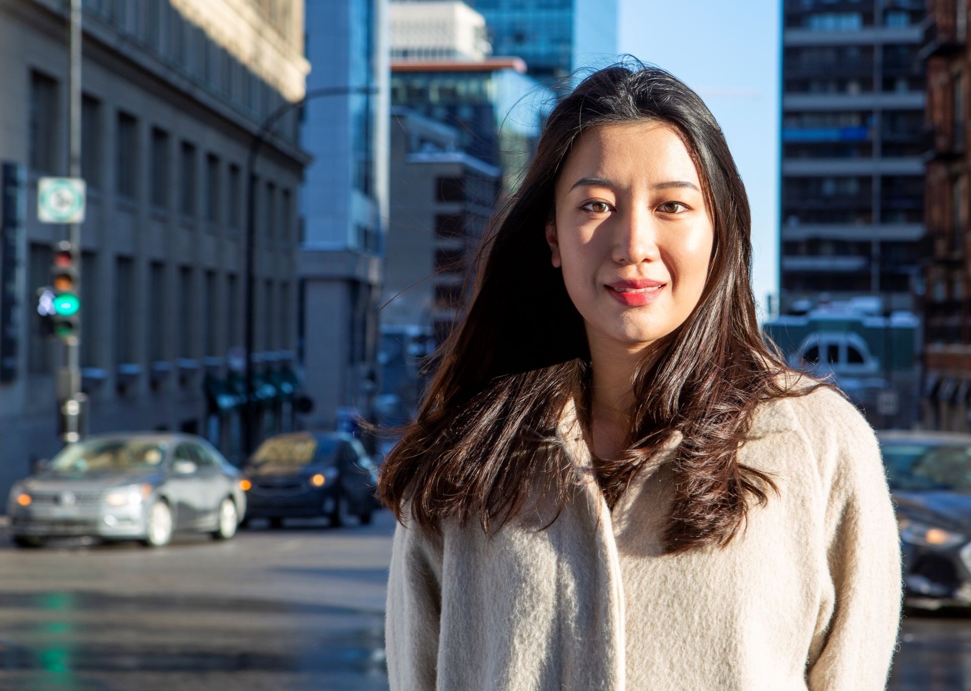 A woman in a white coat stands outside on a city street
