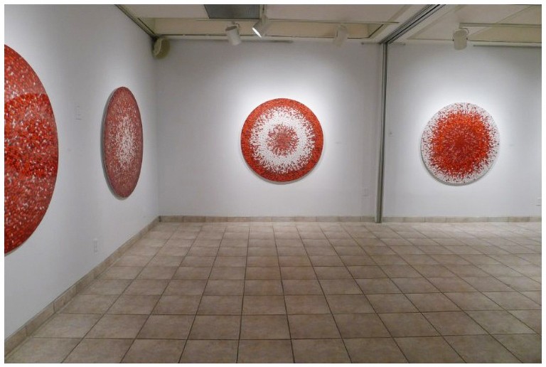 Art pieces — circular, textured, red — exhibited in a gallery