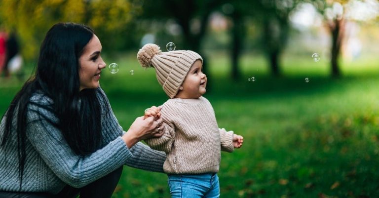 A mother and toddler in a park looking at soap bubbles