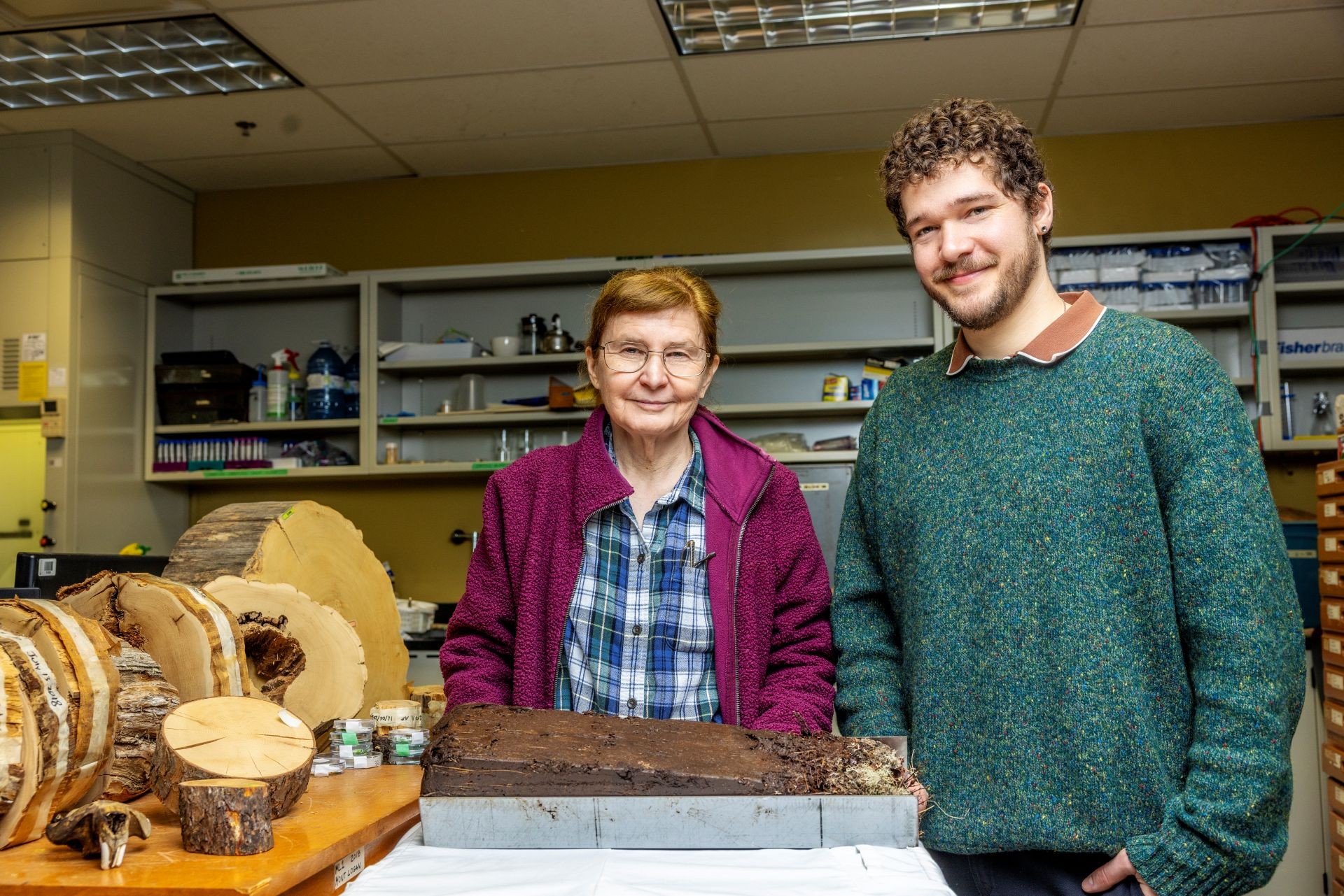 An older female and younger male scientist in a lab with tree rings