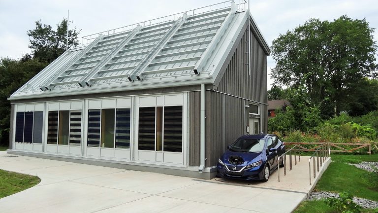 An electric vehilcle parked outside a modern house with a grid of metal bars on its roof and blacked out windows
