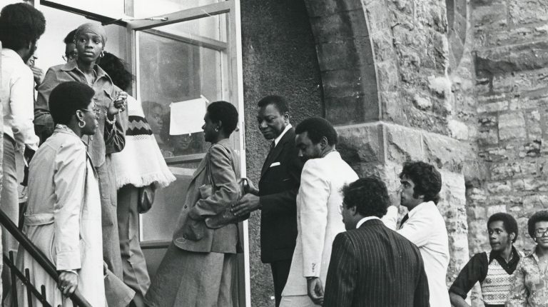 A black and white archival photo of people filing up an outdoor staircase to enter a building.