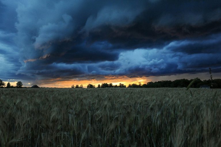 stormy clouds over a large field, with a sunset in the far distance