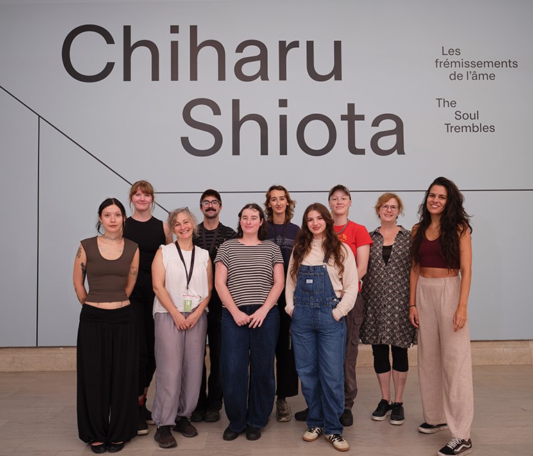 A group of people standing in a line outside an art exhibition and smiling for the camera