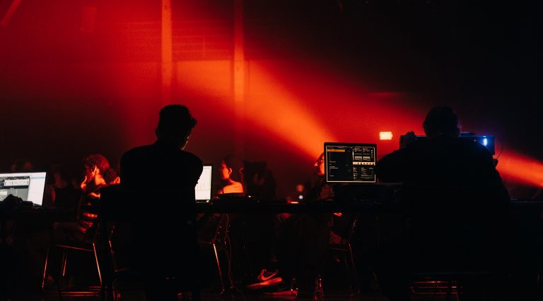 A stage lit in red with electroacoustic musicians giving a performance