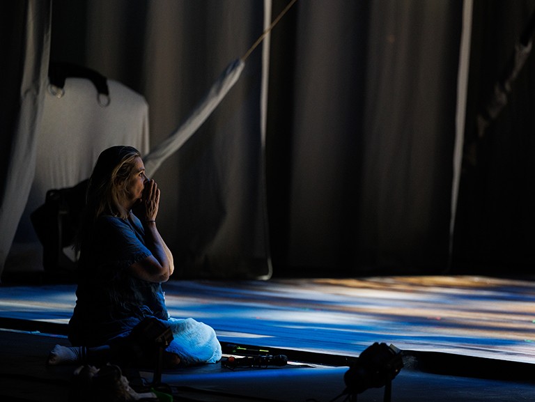 A woman kneeling at the edge of a stage wtih her hands held up to her mouth.