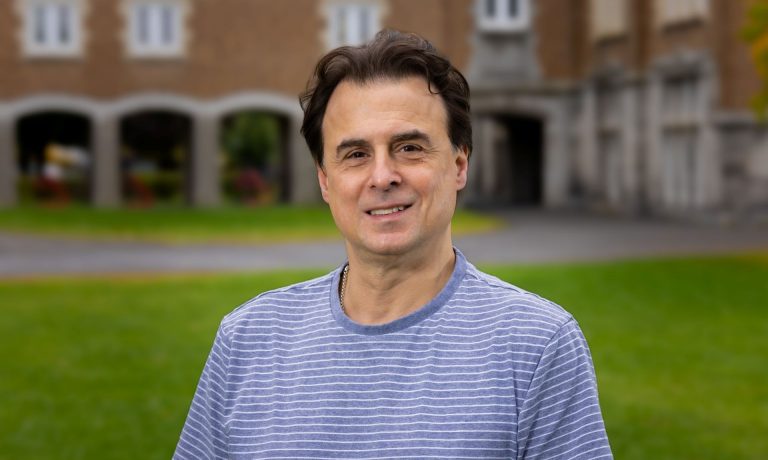 A researcher in a blue shirt standing on a sunny campus