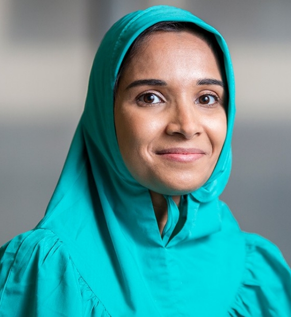 Arwa Hussain pose sur un fond gris, portant un couvre-chef et une tenue bleus