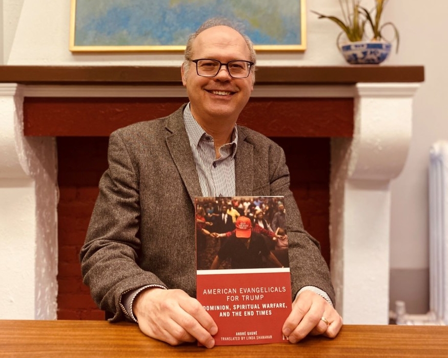 Professeur André Gagné, assis à son bureau, avec son livre entre les mains