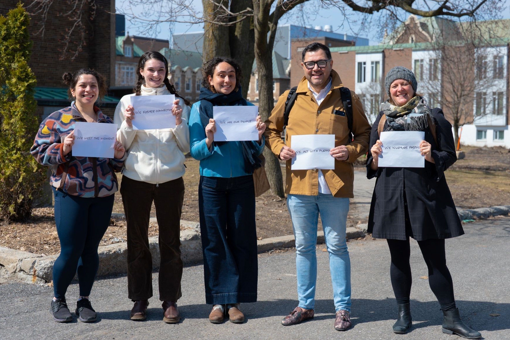 Cinq personnes, debout à l'extérieur sur le campus de Loyola. Chacune tient une feuille blanche sur laquelle est inscrit l'un des engagements.