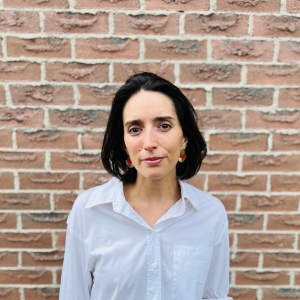 Dark haired woman smiling in front of brickwall