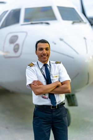 Pilot Amr Yosry stands outside a Calm Air plane, with his arms folded across his chest. 