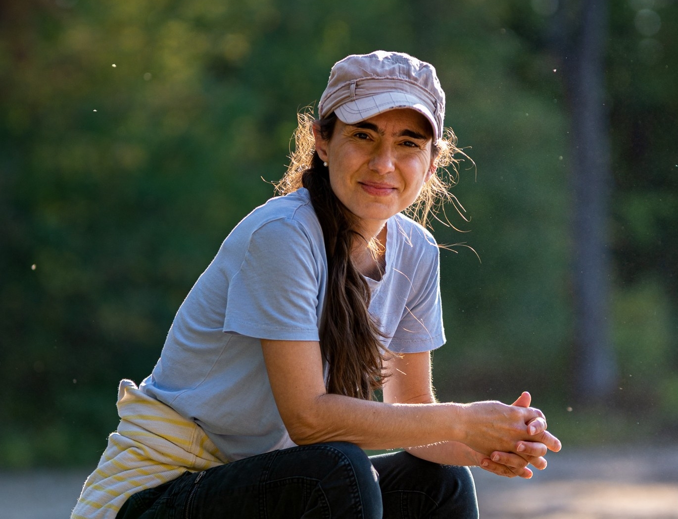 Katherine Jerkovic, crouching down, wearing jeans and a ball cap.