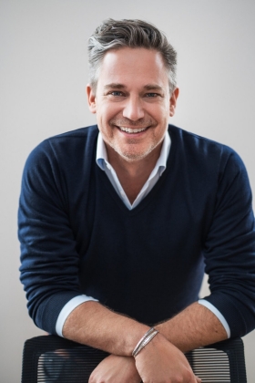 Jean-François Bélisle leans on the back of a chair, smiling