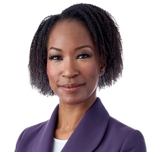 Portrait d'une femme souriante aux cheveux noirs courts portant un blazer violet et un chemisier blanc.